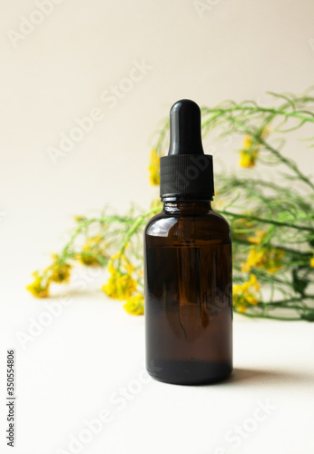 Rapeseed flowers oil in brown glass bottle with pipette on light beige background, vertical. Mockup eco organic natural cosmetic product for skincare, body care or hair care