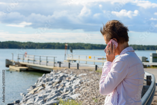 Mature woman talking on the phone by the pier against view of the lake