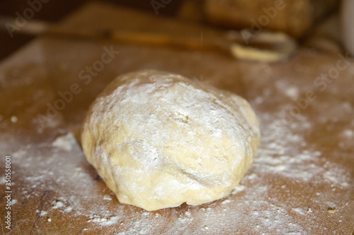 Kneaded dough for bread laying on wooden board. Wheat flour dusted around. Selective focus. Studio shot. Closeup side view. Homemade bakery and nutrition concept