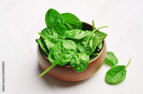 Fresh spinach leaves in dark wooden bowl on white background. Healthy vegan food concept. Eco-conscious vegan lifstyle.