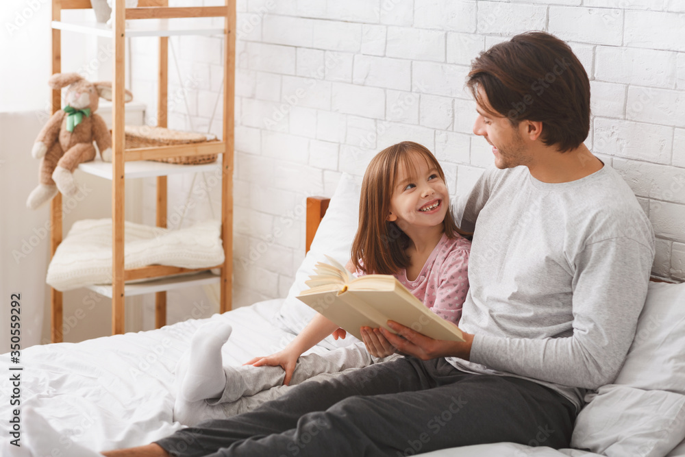 Father and happy daughter reading book in bedroom Father and happy daughter reading book in bedroom
