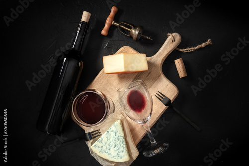 Wine and cheese tasting, shot from above on a black background, with a vintage corkscrew and a bottle