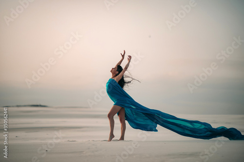 Woman wrapped in blue tissue posing in the desert on sand background. photo