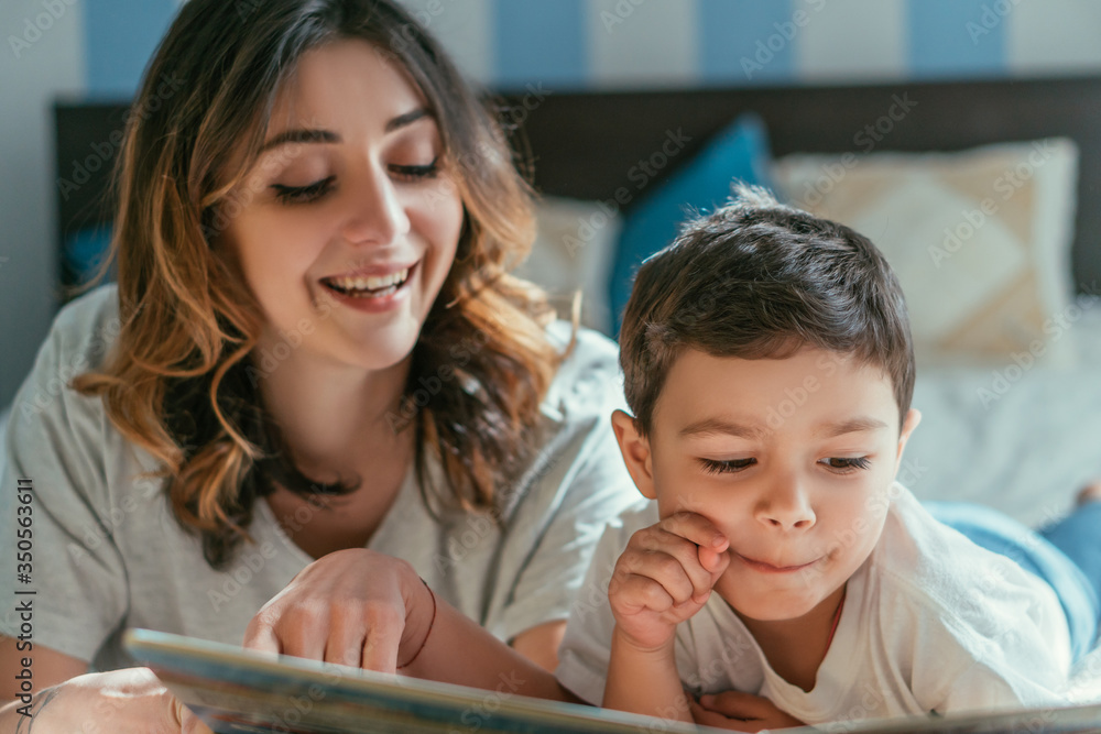 selective focus of toddler boy smiling near mother reading book at home selective focus of toddler boy smiling near mother reading book at home