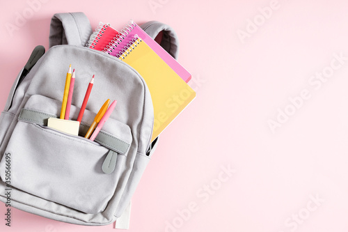 Back to school concept. Backpack with school supplies, pens, pencils, notebook on pastel pink background. Flat lay, top view, copy space photo