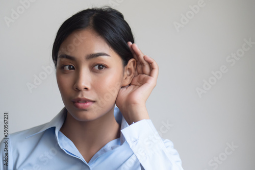 woman listening to something; portrait of southeast asian woman with hearing ear, concept of rumor, gossip, hearing loss, whispering, hard of hearing, fake news, good news, bad news photo