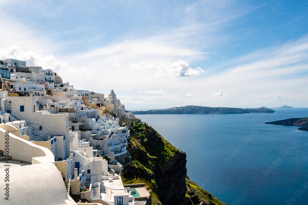 Fototapeta premium Sunshine on white houses near tranquil Aegean sea against sky with clouds in Greece