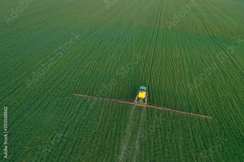 In the spring season, the farmer sprays wheat or barley with insecticides and fungi with a tractor. Top view, aerial view of the mounted tractor while working. Pest County / Hungary - 05.05.2020.