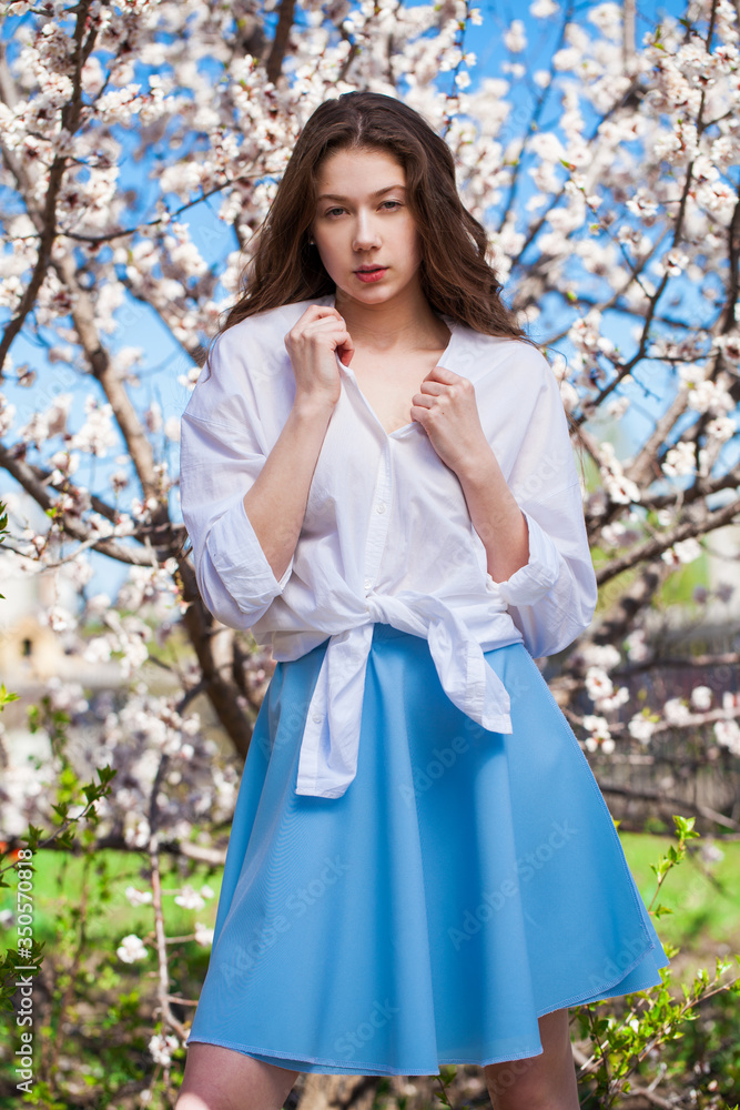 Pretty teen girl are posing in garden near blossom cherry tree with white flowers