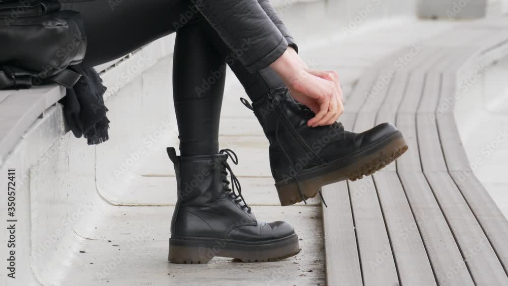 Close up shot of stylish woman tying up her black boots outside, she's addicted to black color Close up shot of stylish woman tying up her black boots outside, she's addicted to black color