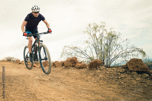Fototapeta Naklejka Na Ścianę i Meble -  Cyclist in violet t-shirt Riding a mountain bike. Man on mountain bike rides on the trail on a stormy day. Extreme Sport Concept - Image
