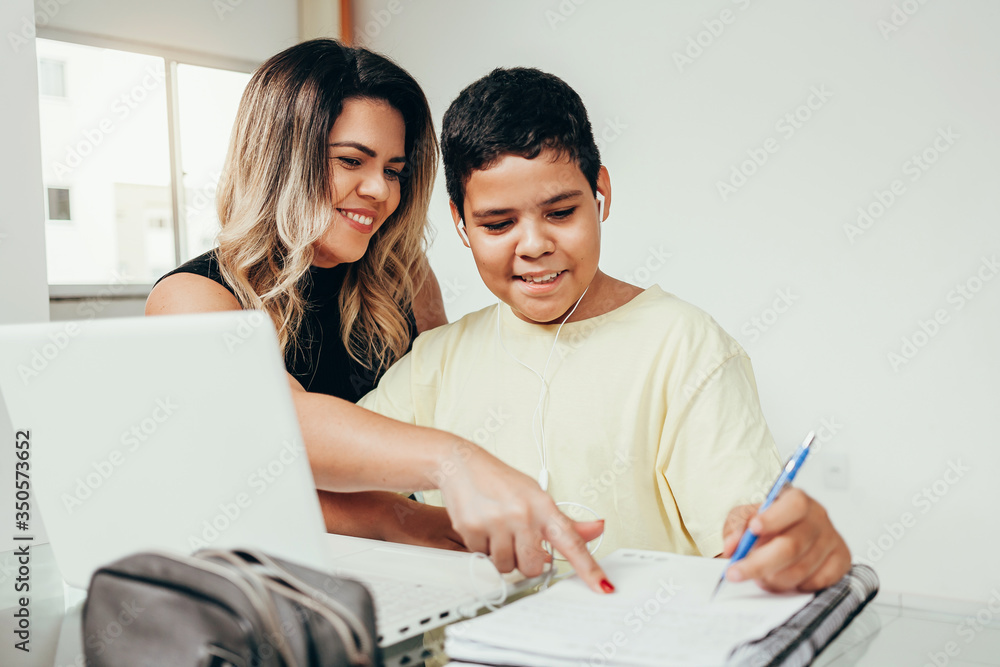 Young student doing homework at home with laptop helped by his mother. Mom teaching his son. Education, family lifestyle, homeschooling concept Young student doing homework at home with laptop helped by his mother. Mom teaching his son. Education, family lifestyle, homeschooling concept