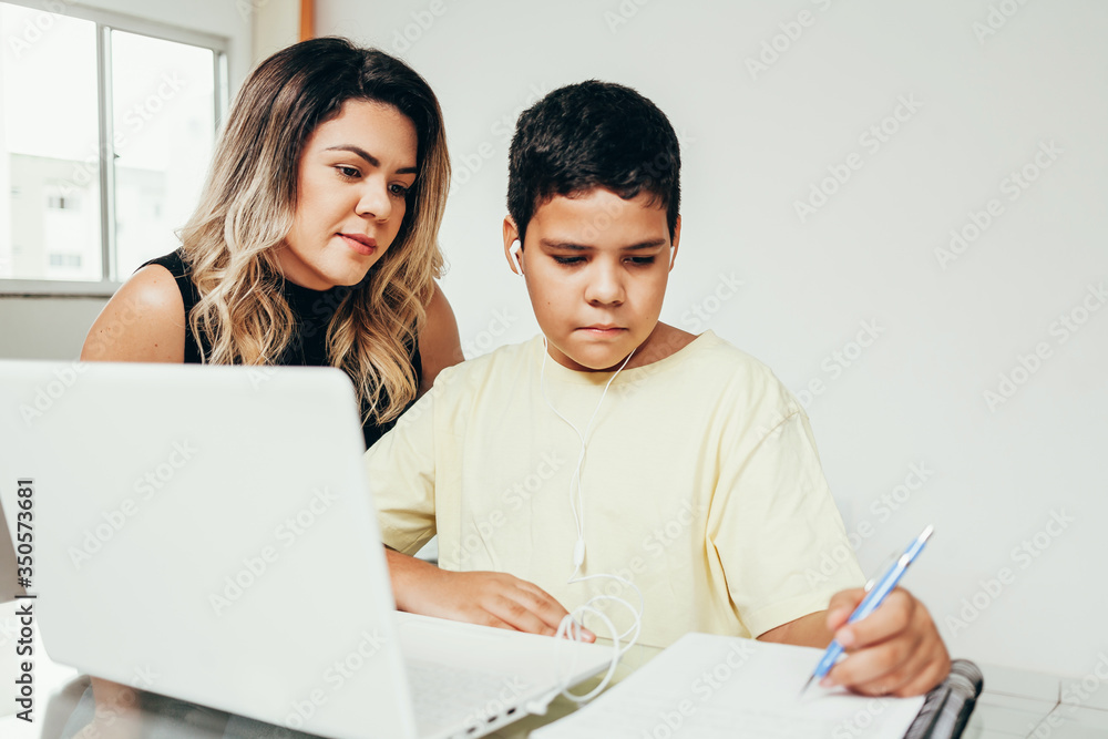 Young student doing homework at home with laptop helped by his mother. Mom teaching his son. Education, family lifestyle, homeschooling concept Young student doing homework at home with laptop helped by his mother. Mom teaching his son. Education, family lifestyle, homeschooling concept