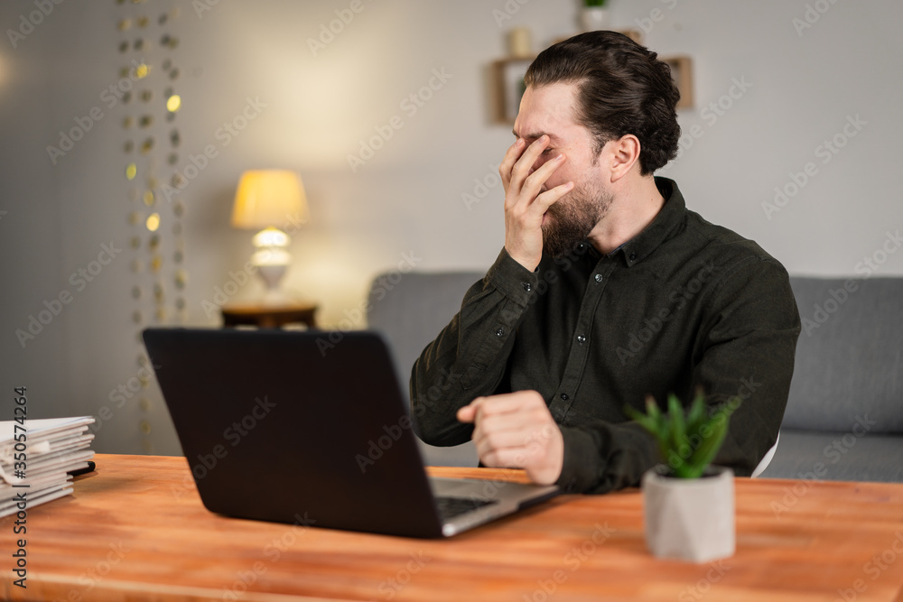 Tired man works at a laptop, works from home. stay at home challenge. He wants to sleep Tired man works at a laptop, works from home. stay at home challenge. He wants to sleep