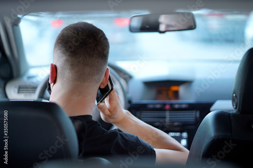 guy a young man in a black t-shirt in a black mask is driving in traffic, talking on the phone, looking out the window, working on the road