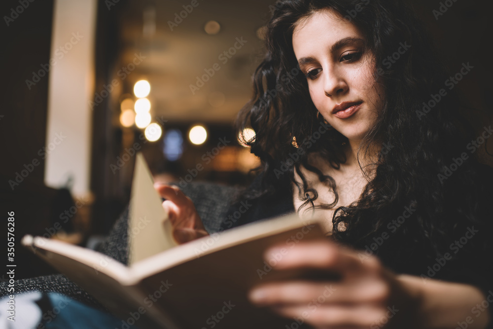 Fototapeta premium Thoughtful young lady reading interesting book in cozy armchair