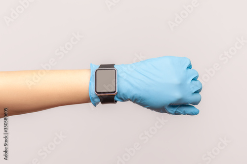 Profile side view closeup of human hand in blue surgical gloves holding and showing wirst smart watch screen. indoor, studio shot, isolated on gray background. photo