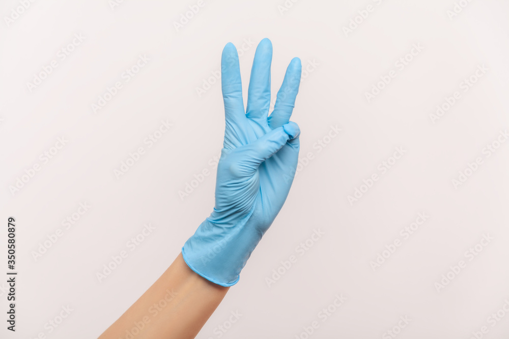 Profile side view closeup of human hand in blue surgical gloves showing number 3 three with hands. indoor, studio shot, isolated on gray background. Profile side view closeup of human hand in blue surgical gloves showing number 3 three with hands. indoor, studio shot, isolated on gray background.
