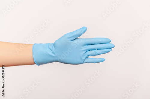 Profile side view closeup of human hand in blue surgical gloves giving hand to greeting or touching. indoor, studio shot, isolated on gray background.