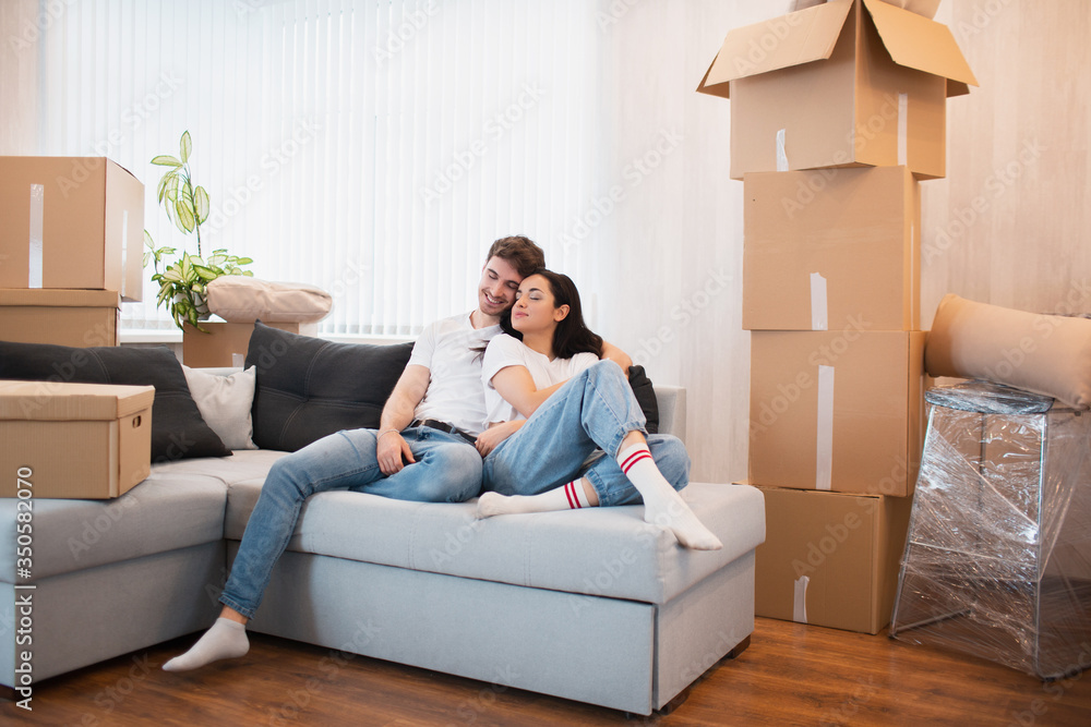 a happy young married couple moves to new apartment. They are sitting on the sofa and looking at their new home. a happy young married couple moves to new apartment. They are sitting on the sofa and looking at their new home.