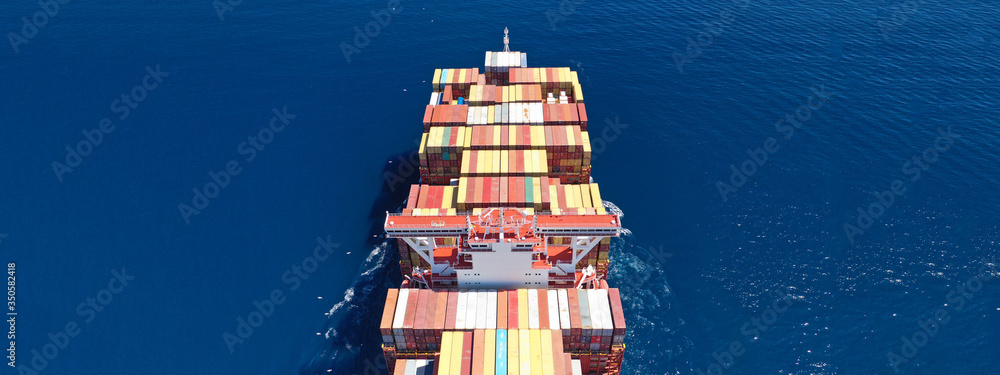 Fototapeta premium Aerial ultra wide photo of Container cargo Ship carrying load in truck-size colourful containers in deep blue open ocean sea 