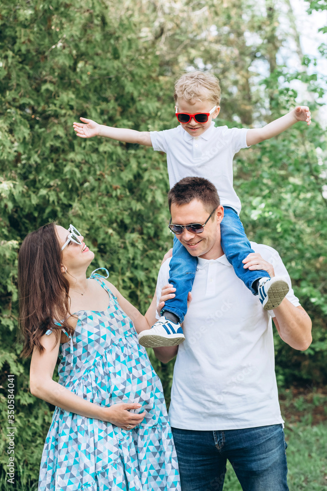A young family and a son walk in nature. Husband and pregnant wife in spring park. happy family outdoor holidays. A young family and a son walk in nature. Husband and pregnant wife in spring park. happy family outdoor holidays.