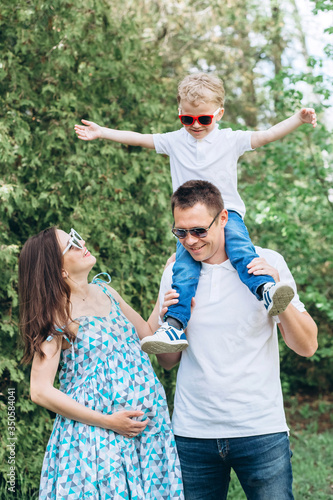 A young family and a son walk in nature. Husband and pregnant wife in spring park. happy family outdoor holidays.