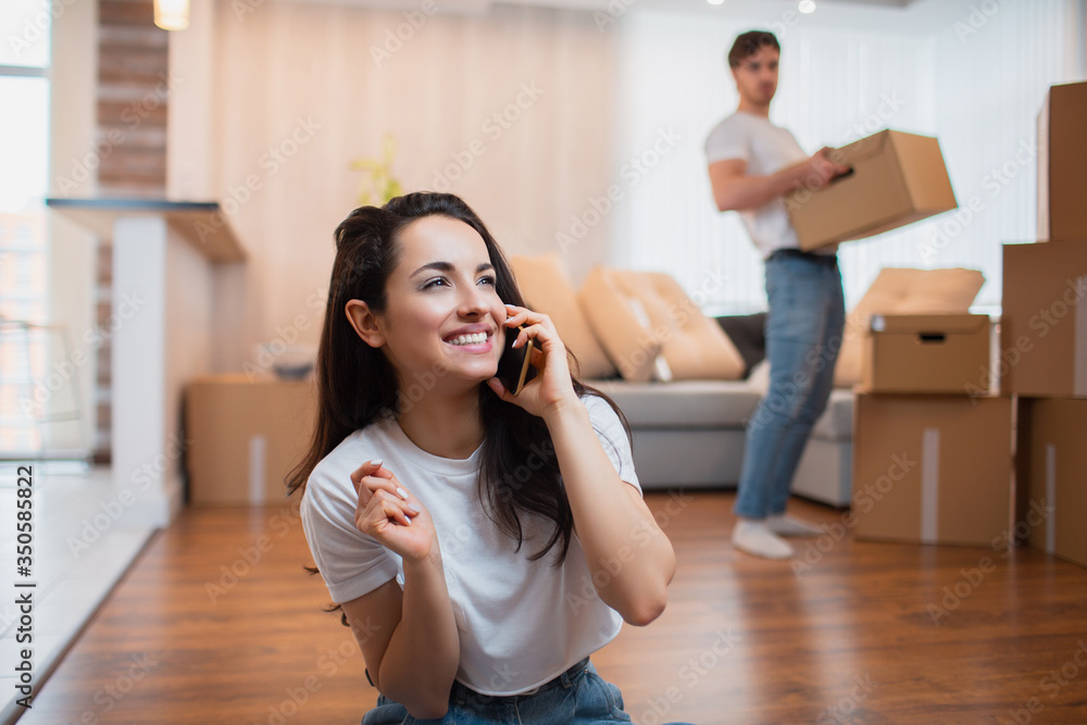 The husband carries boxes, and the wife speaks on the phone