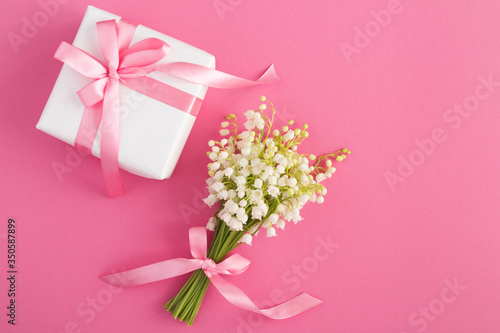 Bouquet of lilies of the valley  with pink bow and white gift box on the pink  background. Top view. Copy space.