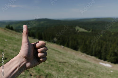 Thumb up close up on a background of a mountain landscape.