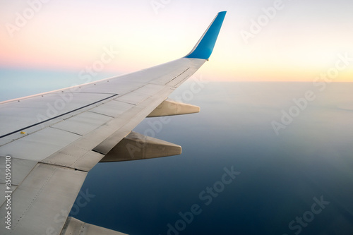 View from airplane on the aircraft white wing flying over ocean landscape in sunny morning. Air travel and transportation concept.
