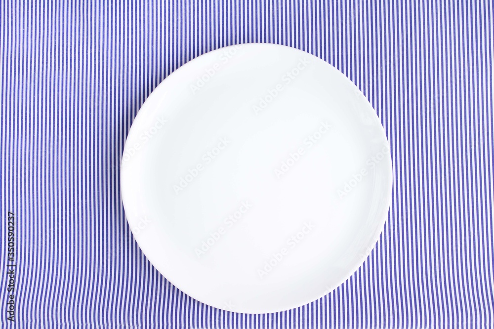 White plate on a kitchen napkin with stripes on a white background, copy space for text, flat lay, top view