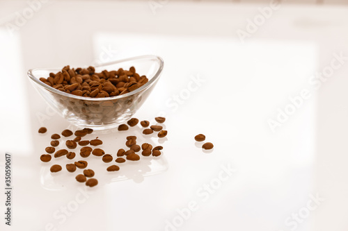Coffee beans in a glass bowl on a glossy light table with reflection. some grains are scattered on the table. breakfast concept