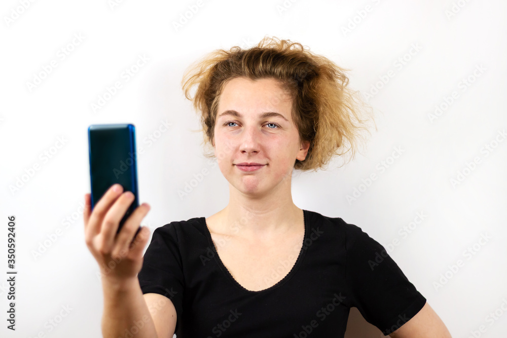 A girl with yellow hair is talking on a video link on a smartphone and looks at the phone screen with a surprised question on a white background. Modern technologies, youth, emotions A girl with yellow hair is talking on a video link on a smartphone and looks at the phone screen with a surprised question on a white background. Modern technologies, youth, emotions