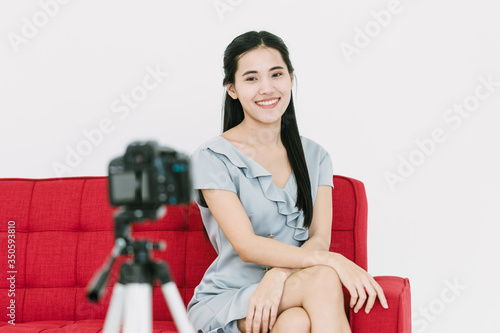 Long Black hair Thai woman model sitting on Red sofa to self portrait with Camera on Tripod with smile face and looking  to the camera © jiradet_ponari