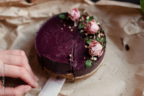 The hand cuts the cake with a knife. Purple cake. The cake is decorated with flowers. 
