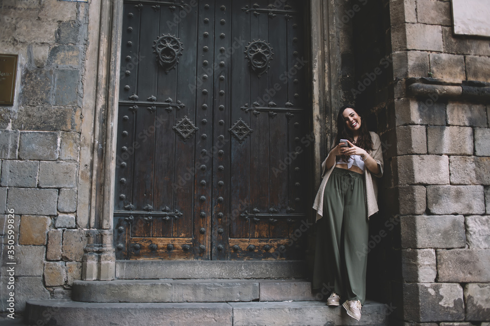 Cheerful young woman using smartphone on street at entrance of ancient building in old town Cheerful young woman using smartphone on street at entrance of ancient building in old town