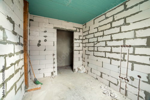 Interior of an apartment room with bare walls and ceiling under construction. © bilanol
