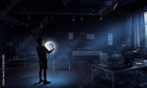 Boy holding moon at night in the office