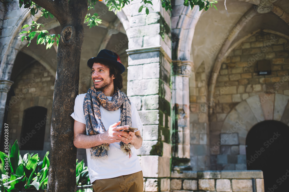 Obraz premium Positive male tourist standing next old building with smartphone