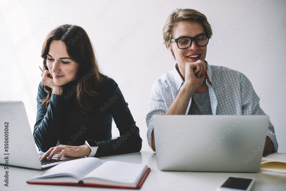 Cheerful caucasian hipster guy watching webinar on laptop computer enjoying learning in business school while his female colleague sitting near, positive freelancers enjoying remote job earn online. Cheerful caucasian hipster guy watching webinar on laptop computer enjoying learning in business school while his female colleague sitting near, positive freelancers enjoying remote job earn online.