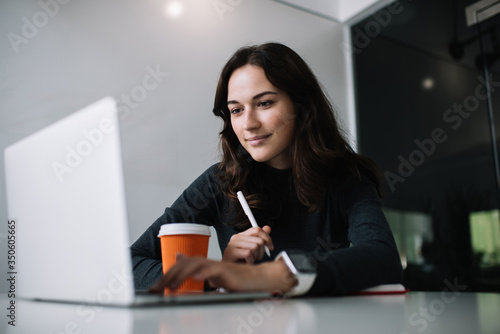 Young caucasian brunette woman using laptop computer for researching information for startup business, skilled female freelancer using app on netbook and 4G working remotely in coworking space photo