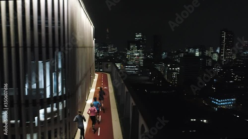 Group of runners running around rooftop running track at night with London skyline