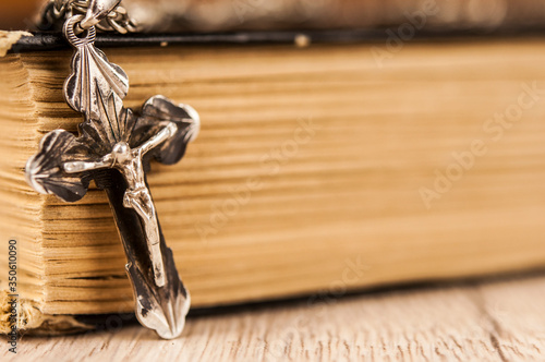 Closeup of Christian cross with silver chain on blank open book with a black wooden background