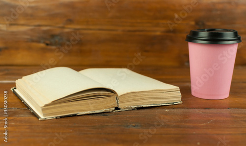 Disposable coffee cup with open book on wood table