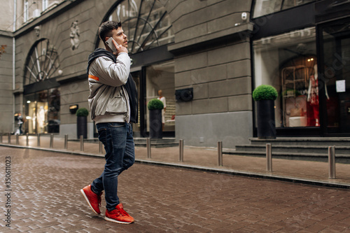 Portrait of happy young man walking on the street and looking aside while talking by his phone.
