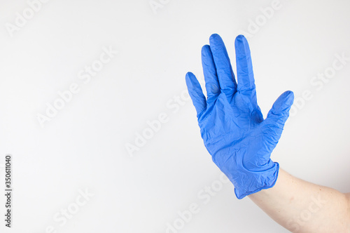Doctor hand in sterile gloves showing sign on white wall background. Pandemic, security. Copy space