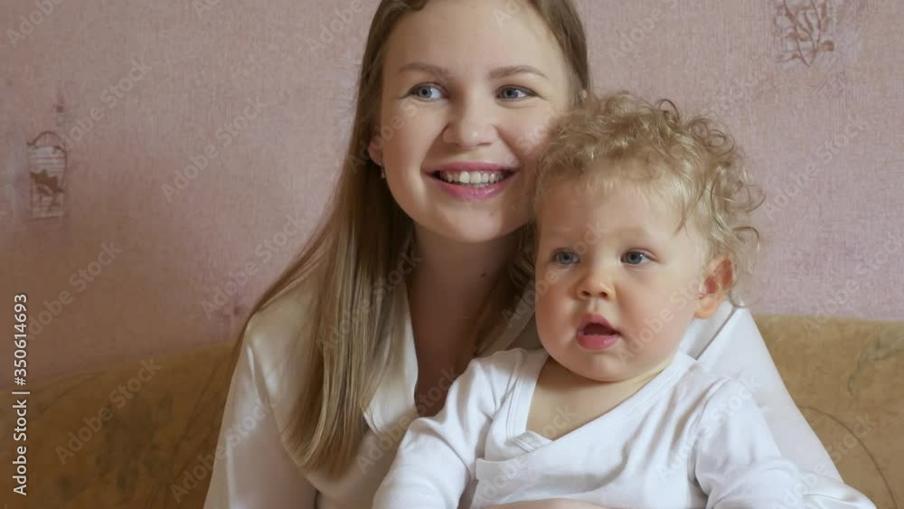 Beautiful attractive mother with a cute baby sits at home on the couch and has fun watching TV. Close-up. Beautiful attractive mother with a cute baby sits at home on the couch and has fun watching TV. Close-up.