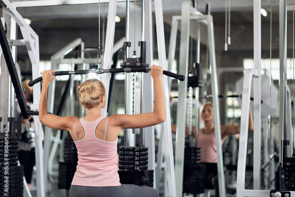 Strong woman exercising with pulldown machine in a fitness club, doing exercises in gym Strong woman exercising with pulldown machine in a fitness club, doing exercises in gym