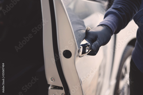 Close up hand pulling the handle of a car thief wearing black clothes and glove stealing automobile trying door handle to see if vehicle is unlocked trying to break into. 